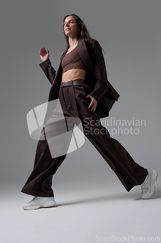Image of Stylish woman in brown pinstripe suit performing wide step in front of camera