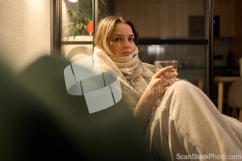 Image of Female with scarf sitting on sofa holding water and smartphone