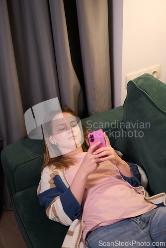 Image of Female lying on sofa looking at smartphone indoors