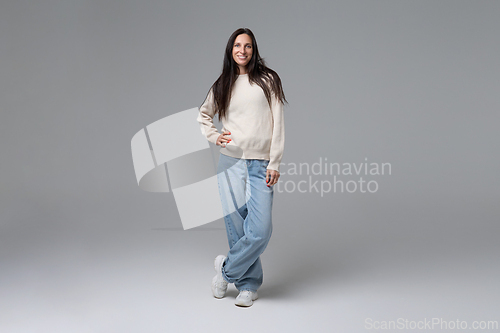 Image of Happy woman posing in white sweater and blue jeans on grey background full length