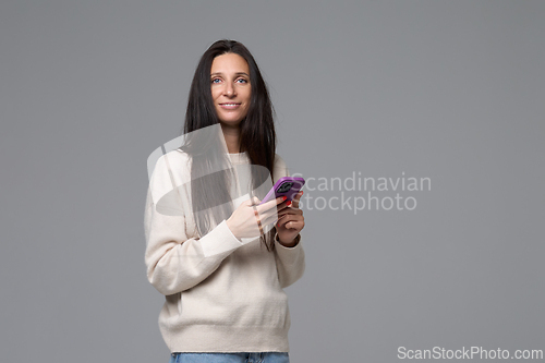 Image of Portrait of woman with smartphone looking at camera isolated on grey background