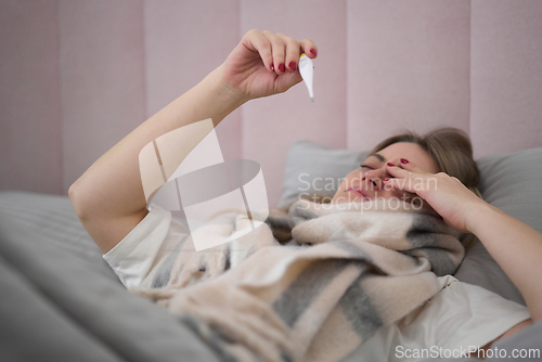 Image of Unwell Woman Monitoring Fever in Soft Bedroom Light