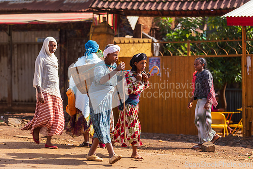 Image of women in traditional dress walk along a dusty street in Demebecha, one carrying a large woven basket. Dembecha, Ethiopia