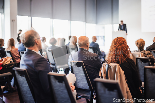 Image of Speaker giving a talk in conference hall at business event. Rear view of unrecognizable people in audience at the conference hall. Business and entrepreneurship concept.