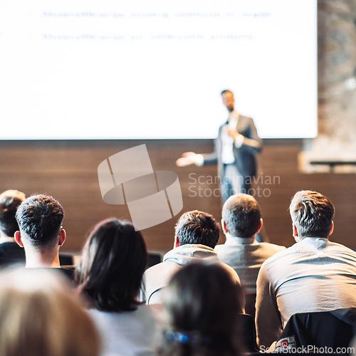 Image of Speaker giving a talk in conference hall at business event. Rear view of unrecognizable people in audience at the conference hall. Business and entrepreneurship concept.