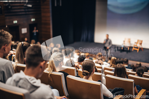 Image of Speaker giving a talk in conference hall at business event. Rear view of unrecognizable people in audience at the conference hall. Business and entrepreneurship concept.
