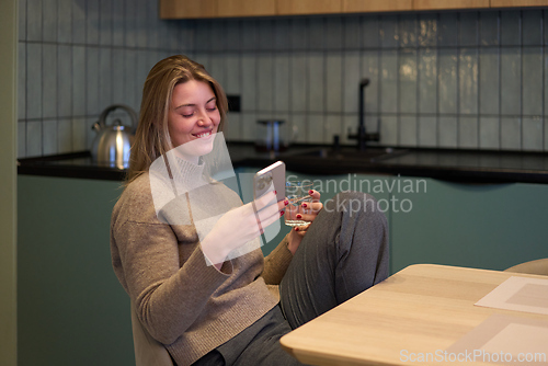 Image of Smiling at Her Phone During a Lighthearted Kitchen Break