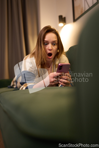 Image of Woman lying on green sofa looking surprised at phone screen