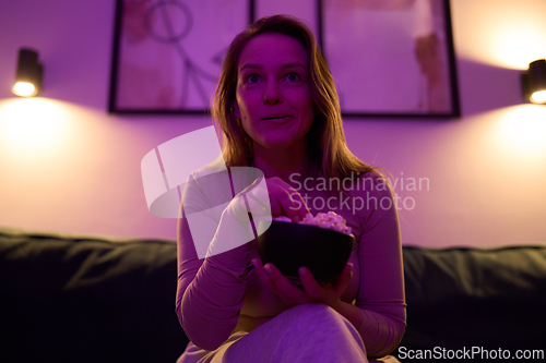 Image of Female watching screen and holding popcorn bowl on sofa indoors