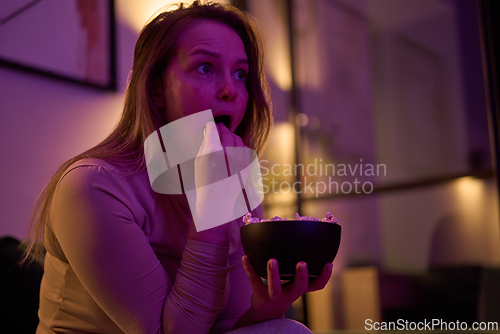 Image of Woman watching screen and eating popcorn at home