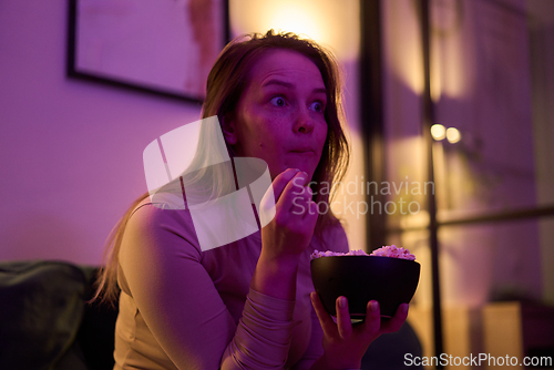 Image of Female holding popcorn bowl while watching screen indoors
