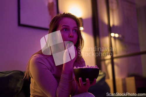 Image of Adult female watching screen and holding popcorn bowl indoors