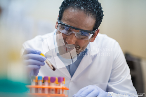 Image of Medical professional in lab analyzing blood sample with test tubes and protective goggles