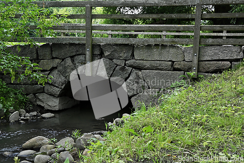Image of A rustic stone bridge with a wooden railing spans a small creek 