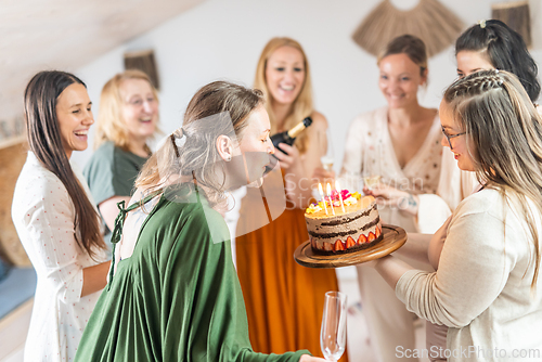 Image of Group of cheerful female friends celebrating personal success stories. Smiling girls toasting with glasses of champagne one holding a birthday cake with candles to blow