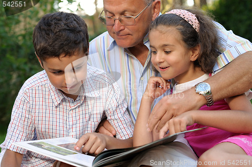 Image of Grandfather and kids reading book outdoors