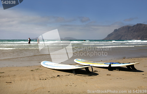 Image of Two surfboards on sandy beach with ocean in background
