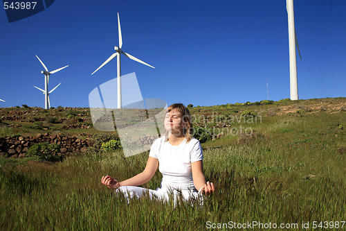 Image of young blond woman doing yoga on the grass on a wind farm beneath