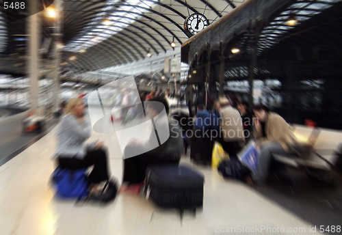 Image of Zoom blurred image of people waiting for trains on Newcastle-upon-Tyne central station, UK, the zoom centred on station clock showing one o'clock 13.00 hrs