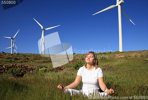 Image of young blond woman doing yoga on the grass on a wind farm beneath