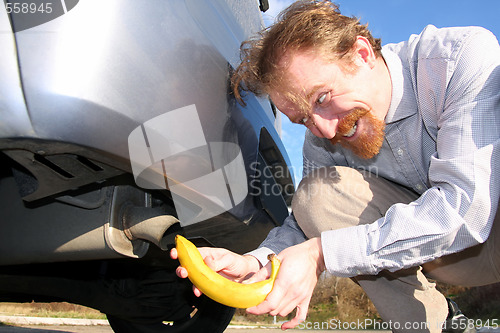 Image of Man putting banana into car exhaust