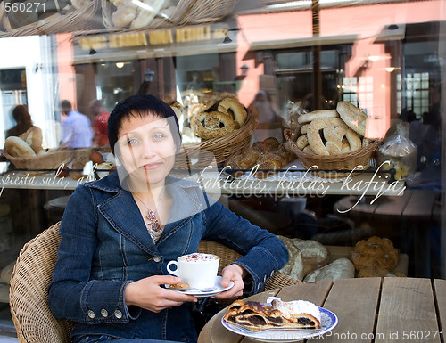 Image of Young beautiful woman with a cup of hot cappuccino at a cafe