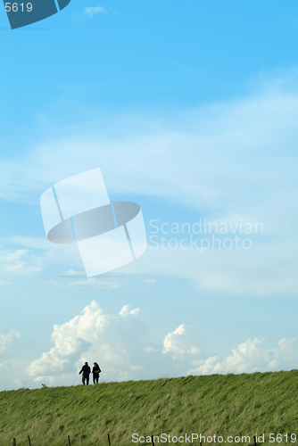 Image of Two people male and female walking on a grass embankment against a big sky background