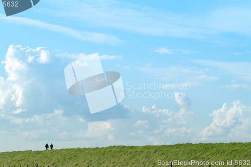 Image of Two people male and female walking on a grass embankment against a big sky background