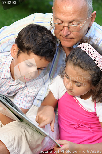 Image of Grandfather and kids reading book 