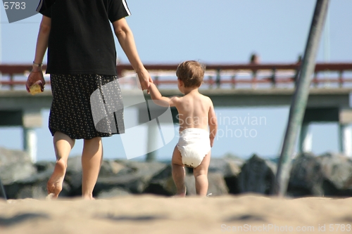 Image of A toddler holds his mother's hand as he heads home from the beach.