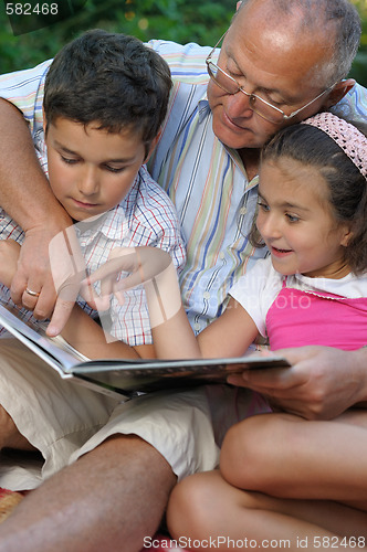Image of grandfather and kids reading book outdoors