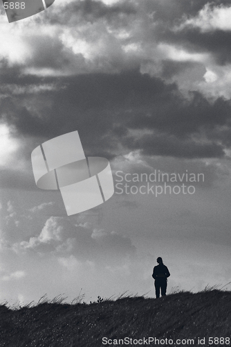 Image of Monochrome lone walker (female) against large menacing sky, with slight added film grain for effect.