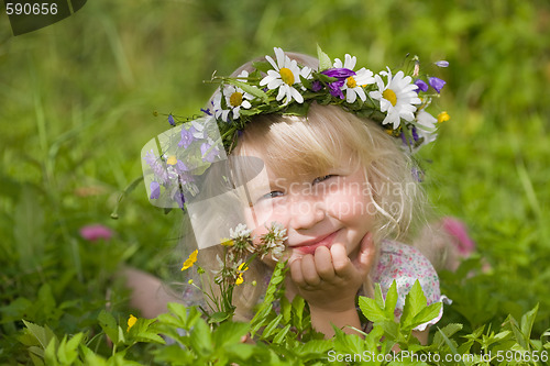 Image of happy little girl in flowers wreath lying on green grass