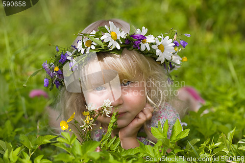 Image of happy little girl in flowers wreath lying on green grass