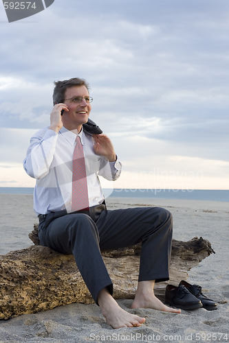 Image of Smiling businessman making a phone call on a beach