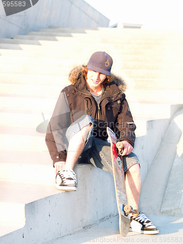 Image of Modern teenager sitting with skateboard in hand