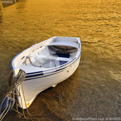 Image of A small row boat beached on the shore at sunset - Cadaques, Spain