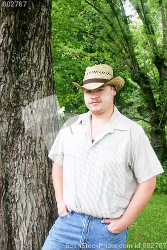 Image of Young cowboy standing beside the tree