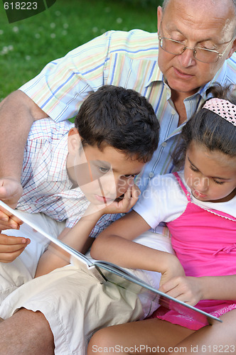 Image of Grandfather and kids reading book outdoors