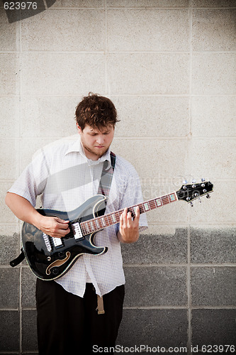 Image of man playing guitar against wall