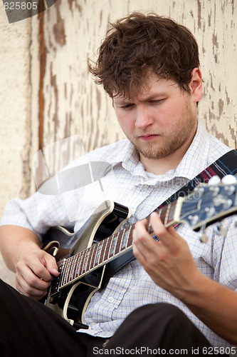 Image of young man playing guitar outdoors