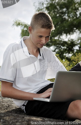 Image of Young man using laptop in a park