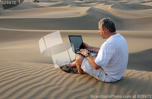 Image of Man with laptop sitting in the desert.