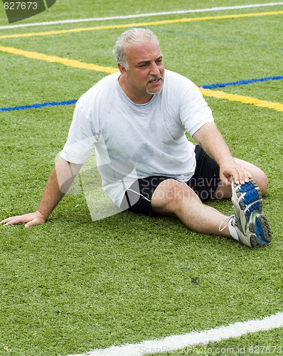 Image of middle age man stretching and exercising on sports field