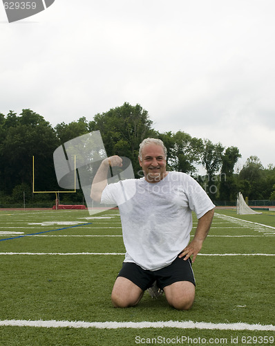 Image of middle age man stretching and exercising on sports field