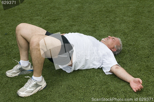 Image of middle age man stretching and exercising on sports field