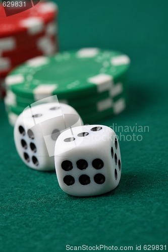 Image of Pair of gambling die and poker chips on a green surface.