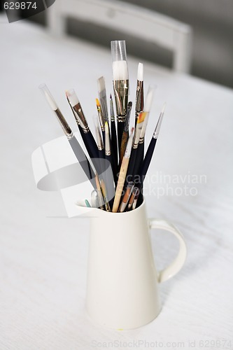 Image of Set of paintbrushes in jug on a table.