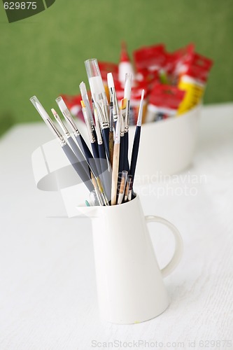 Image of Paintbrushes and tubes of paint on a table outdoors.