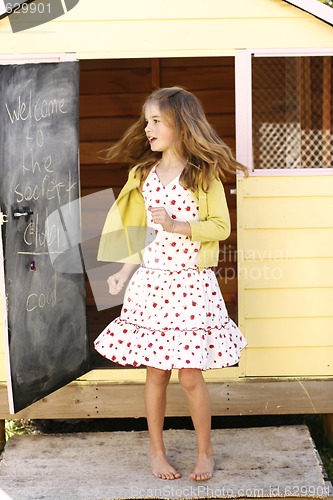 Image of Pretty young girl spinning around outside her playhouse.